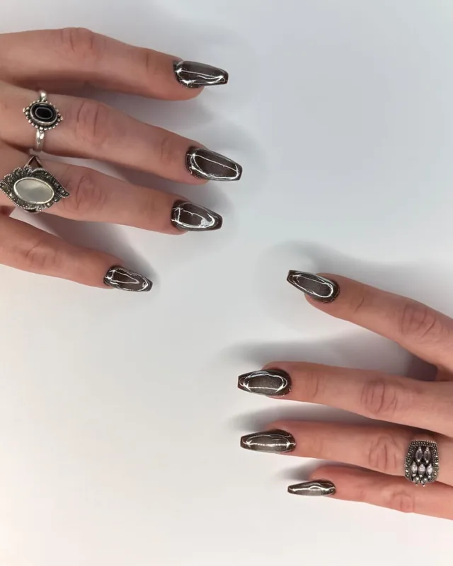 Duas mãos com unhas coffin em cromado grafite, com anéis de prata sobre fundo claro
